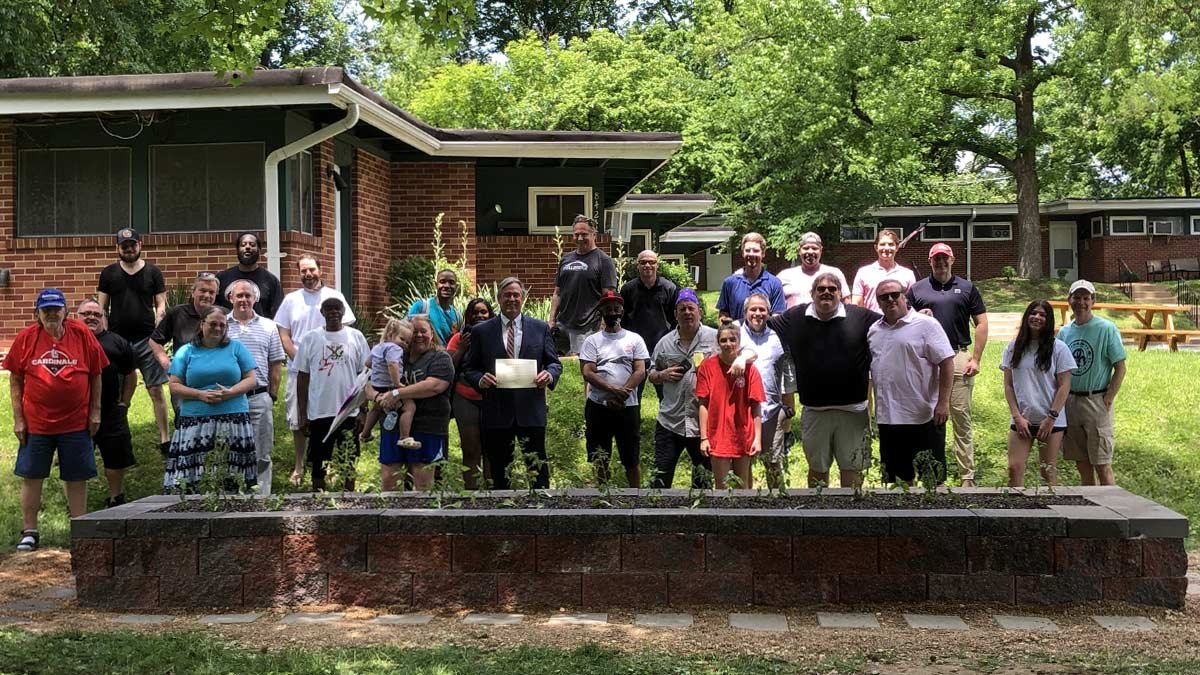Large group of veterans, families, staff and volunteers with Bill outside residence