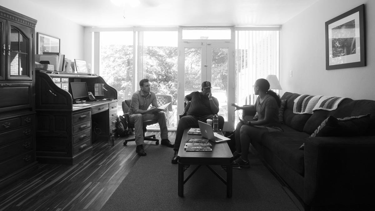 B&W photo of three people sitting in front of the patio door.