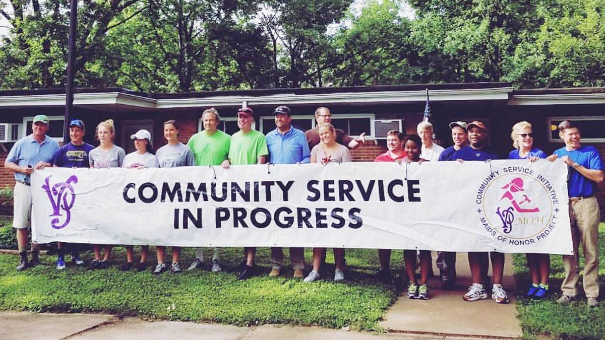 Group of volunteers posing behind Community Service banner in front of the office.